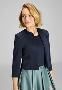 Blazer azul marino con mangas de tres cuartos, diseño elegante y cuello minimalista. Combinado con una falda de teal texturizada que presenta acentos florales.