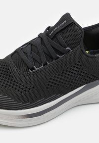 Czarne buty sportowe z oddychającą siateczką, teksturowaną powierzchnią, szarymi sznurówkami i białą podeszwą z subtelnymi szarymi akcentami.