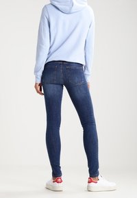 Sudadera con capucha de color azul claro; vaqueros ajustados de color azul oscuro; zapatillas blancas con acentos rojos. Corte entallado, material de algodón, detalles mínimos.