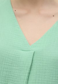 Mint zelena odjeća s teksturiranim, naboranim materijalom. Ima V-izrez s suptilnim naborima na sredini. Mekani, lagani materijal.