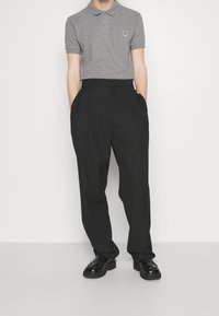 Szary golf z haftowanym wzorem, w zestawieniu z wysokim stanem czarnymi spodniami i czarnymi butami, stojący na neutralnym tle.