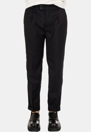 Pantaloni neri su misura con una vestibilità slim, caratterizzati da due bottoni frontali, pinces e orli arrotolati. Abbinati a mocassini neri.