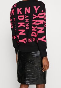 Pull noir avec l'inscription rose "DKNY", texture douce, encolure ronde, assorti à une jupe en cuir synthétique noir effet crocodile, finition lisse.