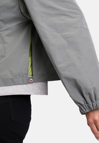 Lichtgrijze waterdichte jas met een elastische manchette, groene voering en een drukknoopdetail aan de zoom.