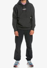 Felpa con cappuccio grigia scura, dotata di tasca frontale e logo, abbinata a pantaloni cargo neri. Indossata con scarpe da atletica multicolori.
