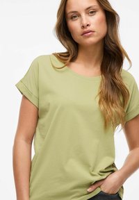 T-shirt vert clair à manches courtes avec un col rond et des manches retroussées, présentant une texture douce et une coupe décontractée.
