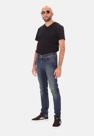 Schwarzes T-Shirt mit V-Ausschnitt, blaue Jeans aus Denim und schwarze Turnschuhe. Runde Sonnenbrille mit metallic Finish. Einfaches und lässiges Design.