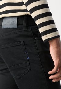 Svarte denimjeans med en lapplomme og kontrasterende blå sømdetaljer. Båret med en stripete langermet skjorte.