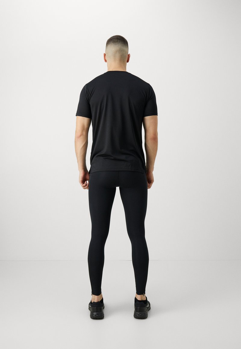 T-shirt noir à manches courtes assorti à des leggings noirs. Le matériau semble lisse et ajusté. Des chaussures de sport noires sont portées.