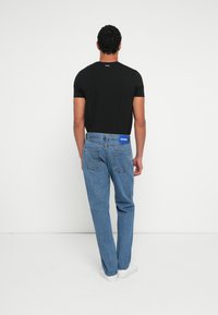 Camiseta negra de algodón con mangas cortas, combinada con vaqueros azules de mezclilla que cuentan con una pretina de marca y corte recto. Zapatillas blancas.