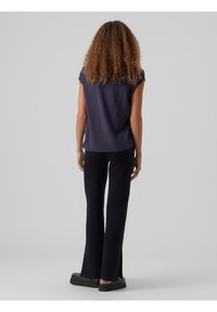 Top de manga corta azul marino combinado con pantalones negros de campana. Los pantalones tienen aberturas laterales y zapatos de deslizar completan el atuendo. Fondo liso.