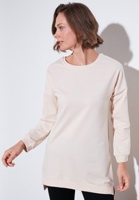 Sudadera de manga larga beige claro con cuello redondo, aberturas laterales, puños acanalados y textura suave y lisa. Adecuada para un uso casual.
