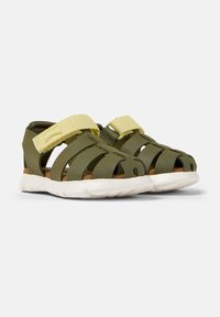 Grön syntetisk sandal med öppen design, elastisk gul rem, vadderad sula och vit gummisula. Har flera utskärningar.