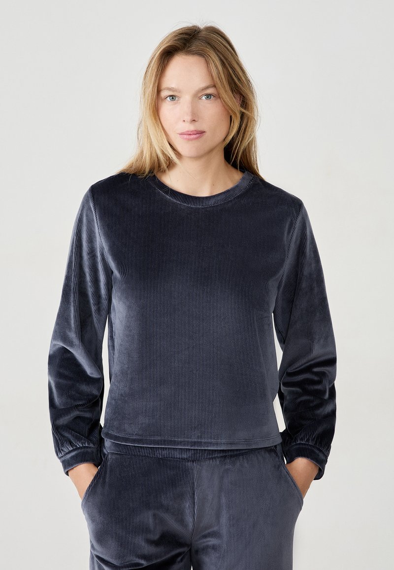 Top lungo in velluto blu navy a maniche lunghe con texture a coste, scollatura rotonda e polsini arricciati. Abbinato a pantaloni coordinati, progettato per il comfort.