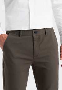 Tummanharmaat housut, jotka on valmistettu sileästä kankaasta. Niissä on etunapit, kaksi sivutaskua ja slim fit -muotoilu.