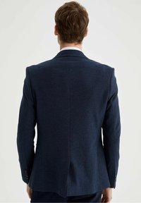 Blazer su misura blu navy in tessuto testurizzato, con spalle strutturate, spacco singolo sul retro e polsini con bottoni.