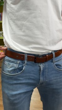 Rjav pas iz usnja z gladko teksturo, z enostavno črno zaponko, nošen z svetlomodrimi jeans hlačami.