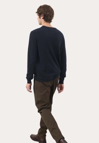 Maglione blu navy con maniche lunghe, scollatura a girocollo e polsini a costine, abbinato a pantaloni marroni e scarpe marroni, visto da dietro.