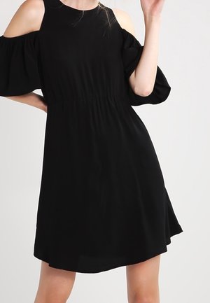 Zwarte jurk met cold shoulder-ontwerp, aansluitende taille en korte uitlopende rok. Gemaakt van lichtgewicht stof; voorzien van vloeiende mouwen en een gladde textuur.