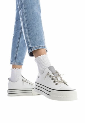 Zapatillas de plataforma blancas con acentos y cordones plateados, suelas de goma texturizadas y una etiqueta de logo. Combinadas con calcetines de caña corta blancos y acanalados.