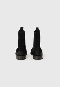 Bottines en daim noir avec des panneaux élastiques sur les côtés et des languettes, dotées d'une semelle lisse et d'une forme épurée.