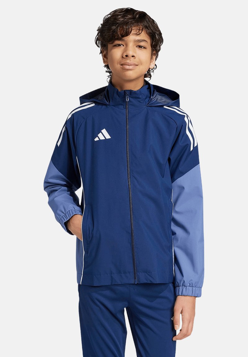 Giacca sportiva blu navy e azzurro chiaro con cappuccio, dotata di strisce bianche sulle maniche e logo sul petto, realizzata in materiale leggero e morbido.