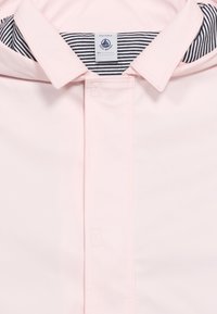 Ροζ ανοιχτόχρωμο γιακά τζάκετ με κρυφή σειρά κουμπιών και ριγέ ύφασμα σε μαύρο και άσπρο στο εσωτερικό του γιακά.