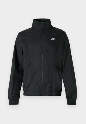 Zwarte Nike lichtgewicht jas met rits, hoge kraag, elastische manchetten en zoom, en een wit Nike-logo op de linkerborst.