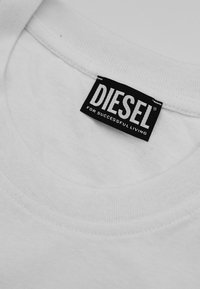 Col montant d'un t-shirt blanc avec une étiquette rectangulaire noire de la marque Diesel indiquant "DIESEL pour une vie réussie" cousue à l'intérieur de l'encolure.