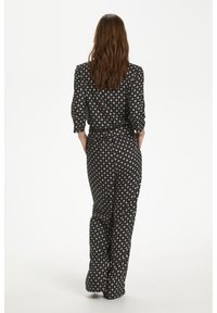 Combinaison noire à motif floral, dotée de manches longues, d'une taille cintrée et de jambes larges pour une coupe décontractée.