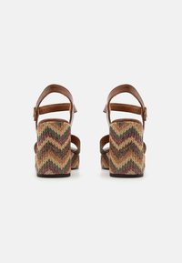 Des sandales en cuir marron avec plateforme présentent un talon en zigzag tissé de couleurs dans des tons terreux. Sangle de cheville réglable pour un ajustement optimal.