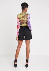 Body s dlouhým rukávem v vícebarevném camouflage designu, spárovaný s černými šortkami na elastický pas a vysokými, šněrovacími botami.