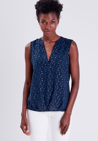 Blouse sans manches marine avec un décolleté en V, motif floral doré et détail de nœud au bas. Fabriquée en tissu léger et lisse.