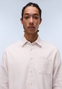 Light-colored striped button-up shirt made of a soft fabric, featuring a chest pocket and a classic collar design.