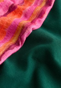 Tissu rayé rose, orange et jaune superposé à un tissu lisse vert foncé, les deux montrant des plis et des textures doux.