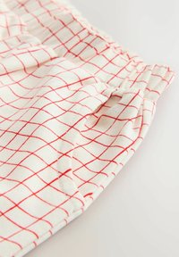 Lys kremfarvet stof med rødt rutemønster, udstyret med elastik i taljen og blød tekstur, designet til komfort og afslappet brug.