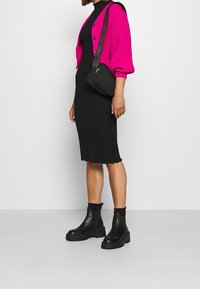 Fuchsie pletený cardigan, černé žebrované šaty s vlnitým lemem, černé kotníkové boty a crossbody taška. Minimalistický styl s texturovanými detaily.