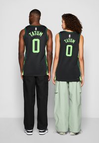 Sorte basketballtrøyer har grønne detaljer, "TATUM" og nummer "0" på baksiden. Bæreren har på seg svarte og mintfargede bredbente bukser.