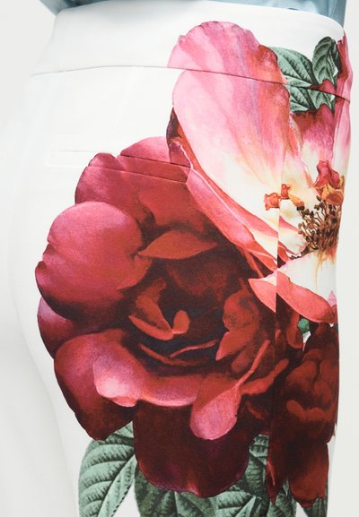 Pantalones blancos con un gran estampado floral detallado de rosas rojas y rosas y hojas verdes en el lado derecho.