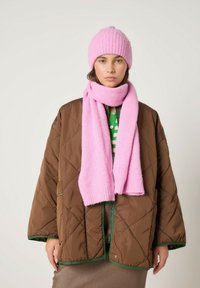 Rožinė pūsta megzta kepurė ir deranti skara kartu su ruda siūta striuke su žalia apdaila. Apranga papildyta žalia raštuota palaidine po apačia.