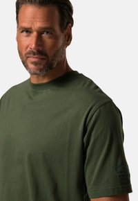 Grøn bomulds t-shirt med rund halsudskæring, korte ærmer og et trykt accent på venstre ærme. Blød tekstur og afslappet pasform.