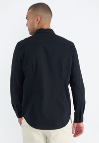 Camisa negra de manga larga con cuello, corte recto y puños abotonados. Tejido suave con un ligero brillo, con un dobladillo redondeado.