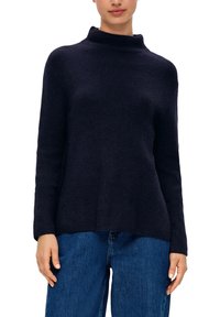 Donkerblauwe ribgebreide trui met een hoge nek en lange mouwen, voorzien van een ontspannen pasvorm en een textuurstof in combinatie met denim jeans.