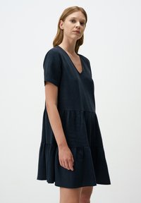 Granatowa sukienka z krótkim rękawem, głębokim dekoltem w kształcie litery V, warstwową spódnicą i luźnym krojem, wykonana z lekkiego materiału o miękkiej teksturze.