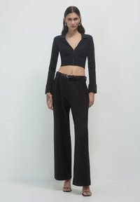Blazer nero corto con maniche lunghe e scollo a V, abbinato a pantaloni neri a gamba larga a vita alta con dettaglio della cintura.