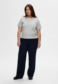Camiseta de algodón gris de manga corta, combinada con pantalones de pierna ancha azul oscuro. Un calzado negro completa el atuendo casual.