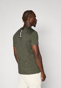 Olive green t-shirt with a textured pattern, short sleeves, a crew neck, and a black label featuring "BORG" on the back.