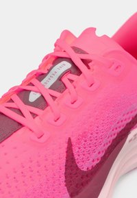 Nike Pegasus juoksukengät, joissa on kirkkaan pinkki verkkopinta, tummempia vaaleanpunaisia yksityiskohtia, synteettisiä päällekkäiskeroksia ja erottuva musta Swoosh-logo.