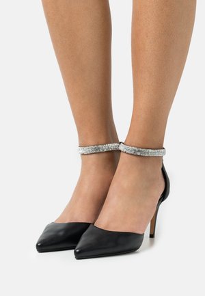 Chaussures à talons hauts en cuir noir avec un bout pointu et une bride de cheville en rhinestones argentés. Texture lisse, talon fin et design minimaliste.