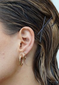 Goldfarbene Metall-Creolen in verschiedenen Größen, getragen an einem Ohr einer Person mit nassem Haar und einer strukturierten Hautoberfläche.